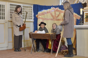 Beim Krippenspiel sitzen Maria und Joseph hinter der Krippe, zwei Hirten stehen links und rechts daneben